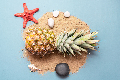 Pineapple, red starfish and pebbles on the sand. Summer vacation abstract background.