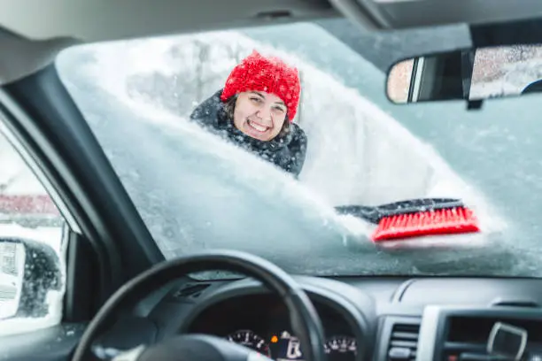 Photo of young pretty woman cleaning car after snow storm