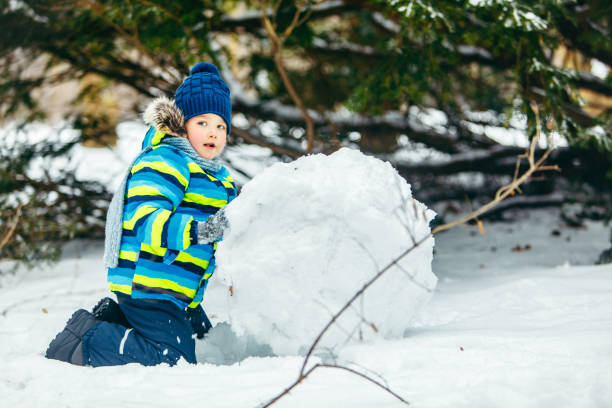 istock little cute boy making snowman. rolling big snowball 1191820606