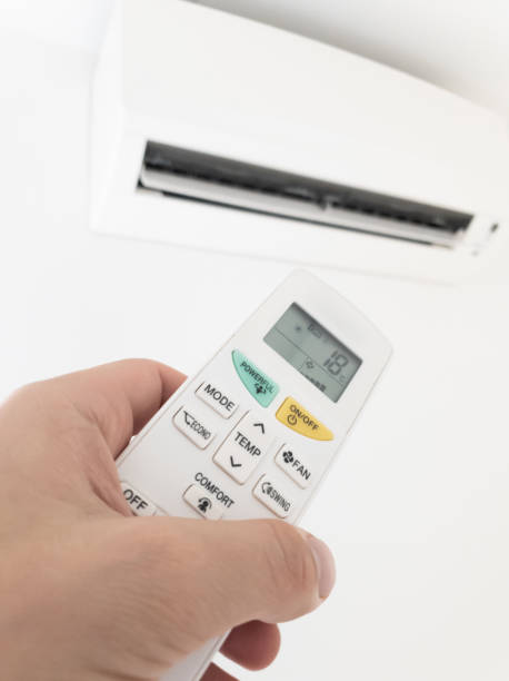istock Modern air conditioner unit with a hand holding a remote. 1191829457