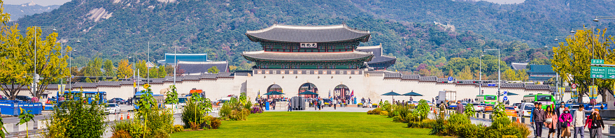Tourists and locals strolling through the Gwanghwamun Plaza overlooked by the Gwanghwamun Gate of Gyeongbokgung Palace and the green slopes of Bukhansan mountain beyond, Seoul, South Korea.