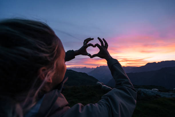 istock Young woman makes heart formation with hands at sunrise 1191837507