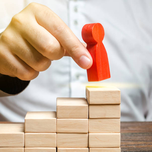 A man puts a red human figure on top of the stairs. Career growth, improvement of skills. Promotion at work of employees to leading post. The concept of success. Training. Education, business un hombre pone una figura humana roja en la parte superior de las escaleras. crecimiento profesional, mejora de habilidades. promoción en el trabajo de los empleados a puestos de liderazgo. el concepto de éxito. entrenamiento. educación, negocios
