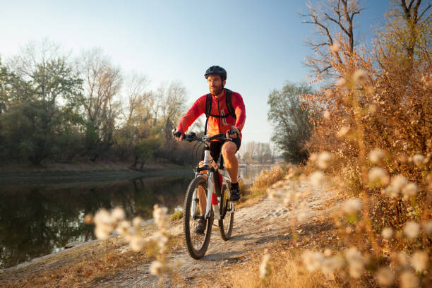 맑은 가을 날에 강가에서 늦은 오후 산악 자전거를 즐기는 행복한 청년 - mountain biking cycling action bicycle 뉴스 사진 이미지