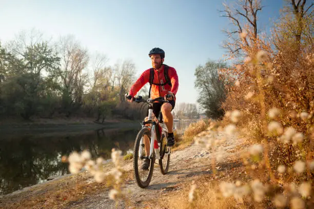 Photo of Happy young man enjoying late afternoon mountain bike ride by the river on a clear autumn day