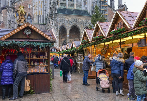 Christmas market in Ulm, Germany Ulm, Germany - December 16, 2017: Christmas market at Munsterplatz square in front of Ulm Minster in overcast day. Fragment of the church's main portal is visible in the background. Upper part of Lowenbrunnen (Lion Fountain) is visible on the left above the market stalls. Unknown people walk around the market stalls and buy sweets and Christmas presents. ulm minster stock pictures, royalty-free photos & images