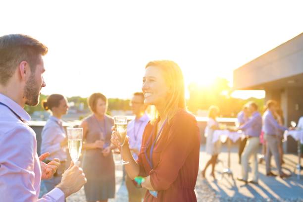 imprenditrice sorridente che beve champagne mentre parla con il collega nella festa di successo sul tetto - drink alcohol summer celebration foto e immagini stock