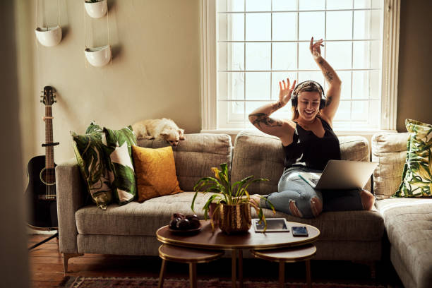 Let the music flow through you Shot of a young woman using a laptop and headphones on the sofa at home people and lifestyle stock pictures, royalty-free photos & images