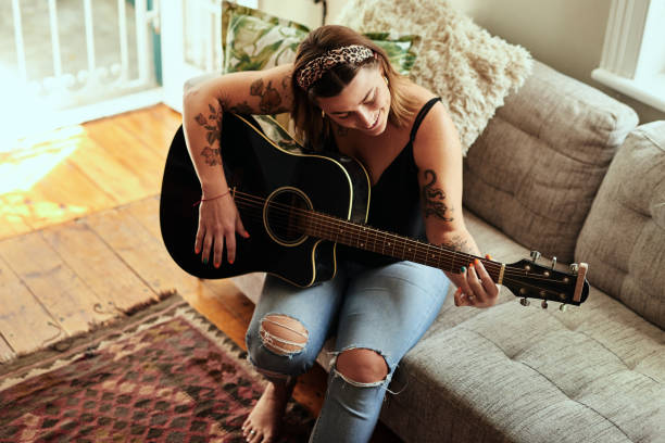 I'm more me with a guitar in my hands Shot of a young woman playing a guitar on a relaxing day at home acoustic guitar tattoos stock pictures, royalty-free photos & images