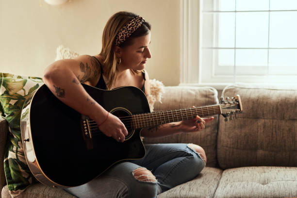 Some people speak in chords Shot of a young woman playing a guitar on a relaxing day at home acoustic guitar tattoos stock pictures, royalty-free photos & images