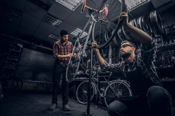 istock Attractive mans are working on bicycle fixing in dark workshop. 1191856554