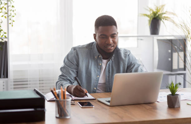 istock Young businessman using laptop and taking notes at worklace in office 1191858832