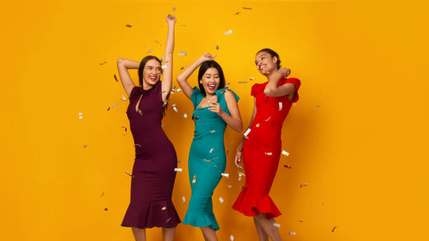 trois filles dansant ayant la partie avec des confettis au-dessus du fond jaune - model3 photos et images de collection