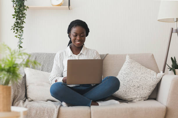 istock Smiling african girl using laptop computer on sofa at home 1191861594