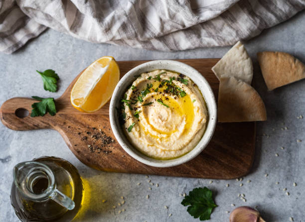 hummus traditionnel de pois chiches faits maison, arrosé d'huile d'olive et de persil frais et de tranches de pita fraîches sur la planche à découper en bois sur fond gris - houmous photos et images de collection