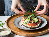 Healthy toast with cream cheese, salmon, fresh cucumber, capers, red onion, black pepper and and an uncertain woman lays on sandwich pea sprouts .