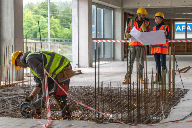 Foreman and forewoman discussing blueprint while worker cutting metal grate