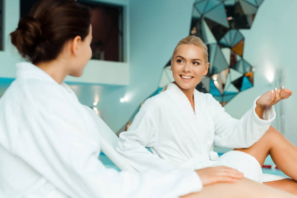 istock attractive and smiling friends in white bathrobes talking in spa 1191874441