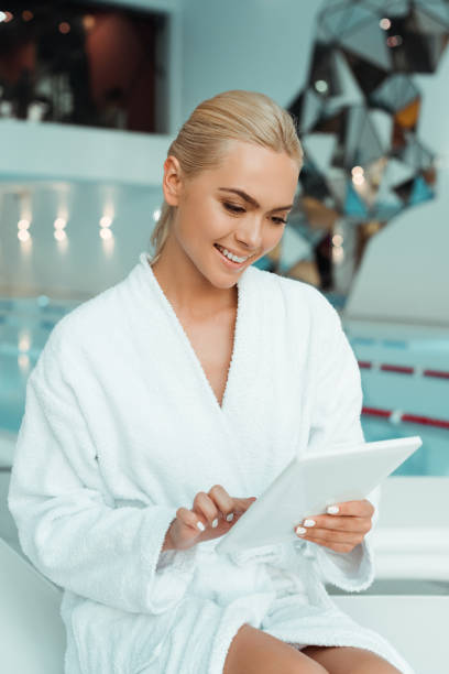 istock attractive and smiling woman in white bathrobe using digital tablet in spa 1191874489