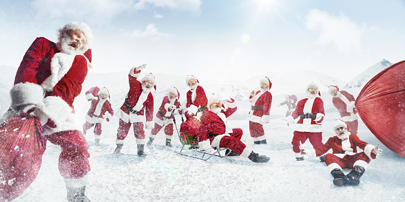 Team of rescuing your Christmas. Santa Clauses pulling bags of presents on sled in snowly winter on background. Caucasian male model in traditional costume. New Year 2020, gifts, holidays, winter mood.