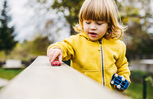Young boy, toddler playing in a public park with his car toys