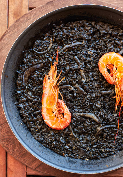 Spanish Black Rice with Cuttlefish and Prawns, called Arroz Negro, on a rustic wooden board.