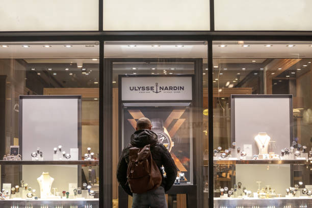 logo d'ulysse nardin devant des montres dans une boutique de détaillant à vienne avec un homme les observant. ulysse nardin est un horloger suisse de luxe. - watchmaking photos et images de collection