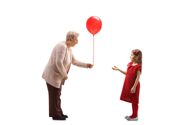 großmutter gibt einem mädchen in einem roten kleid einen roten ballon - child balloon happiness cheerful stock-fotos und bilder