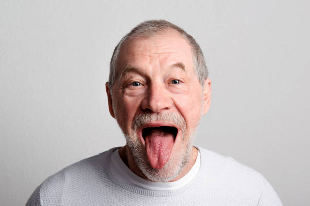 retrato de un anciano alegre en un estudio, sobresaliendo la lengua. - hombre mayor sacando la lengua fotografías e imágenes de stock