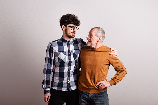 Portrait of a cheerful senior father and young son in a studio, looking at each other.