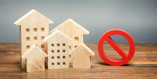 Photo of Wooden houses and a prohibition sign. Inaccessible and expensive housing. Restrictions and a ban on the construction of buildings. Interdictions within settlements. Inaccessibility Index