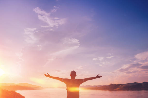istock Happy backpack man raise hand up on sunset sky at river background. 1191884294