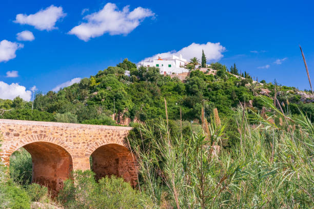 Santa Eulària des Riu, Puig de Missa, Old Town, Ibiza, Spain A low-angle view of the ancient bridge located near the town of Santa Eulària des Riu, on the eastern coast of Ibiza, picturesque clouds, lush vegetation, a glimpse of the small complex of white architectures resting on the top of Puig de Missa, the hill rising near the centre of the town. Developed from RAW. santa eulalia stock pictures, royalty-free photos & images