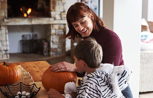 Shot of a happy young mother carving out pumpkins and celebrating halloween with her young son at home