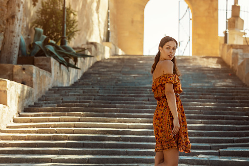 young brunette woman wearing a floral pattern summer dress, standing on a staircase, at a castle in Artà on Mallorca