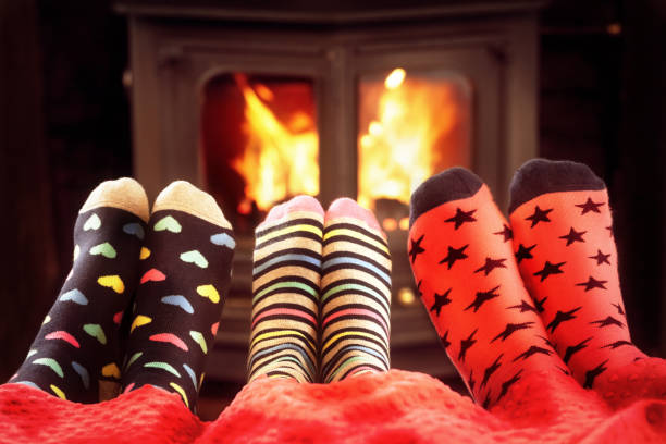 famille dans des chaussettes de laine réchauffant des pieds par le feu en hiver - blanket fireplace winter women photos et images de collection