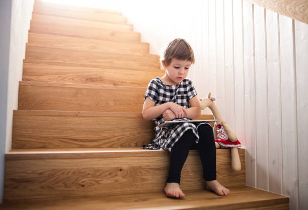 istock A small girl sitting indoors on the stairs, using tablet. 1191896068