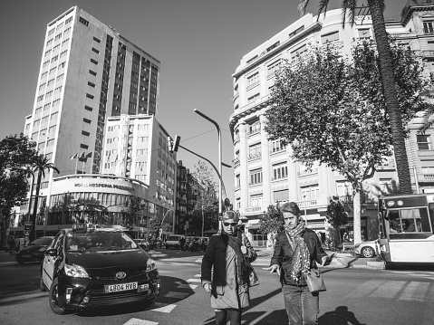 Barcelona, Spain - Nov 2017: Black and white image of Catalan street with two senior women crossing busy avenue in central Barcelona with Hotel Hesperia Presidente in background and taxi car driving