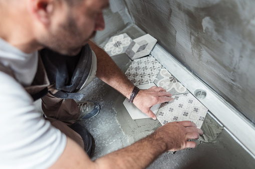 High angle image of male builder installing tiles on the bathroom floor