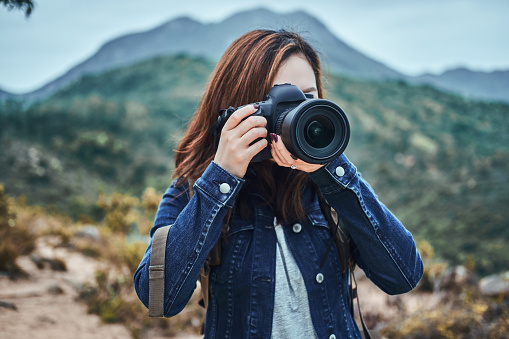 Nature photographer with digital camera is taking a photo shoot of nature. She has denim shirt.