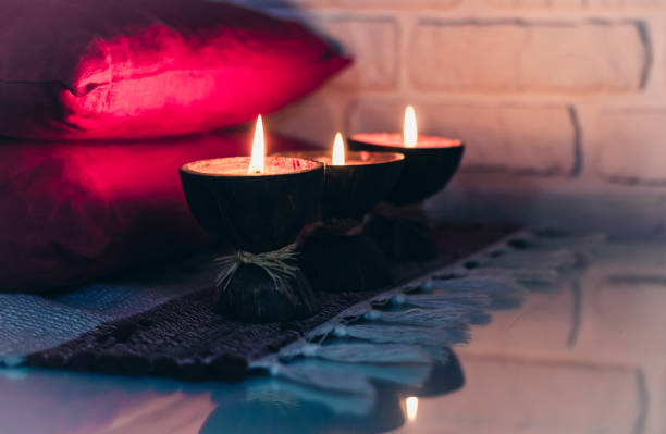 istock Burning spa aroma candle in coconut shell on a knitted multicolored rug and red pillows opposite the white wall, cozy home interior 1191900414