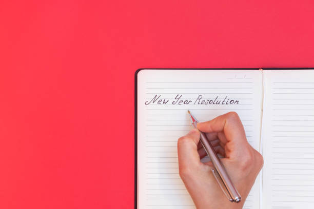 istock Directly above view of woman's hand writing words New Year Resolution in a notepad on red background 1191905669