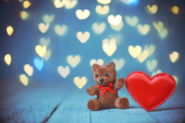 Teddy bear with a heart in his arms sitting on rose petals on a red background for Valentine's Day