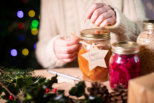 Putting Reusable Wooden Gift Tag On Homemade Jars Of Preserved Fruit For Eco Friendly Christmas Gift