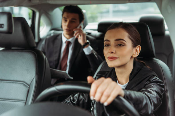 donna tassista in possesso del volante mentre l'uomo d'affari parla su smartphone - driving mobile phone car talking foto e immagini stock