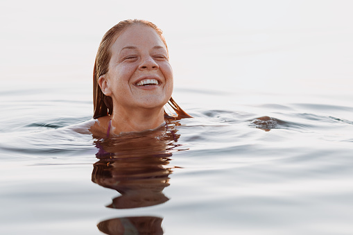 Young happy woman floating in the sea in sunset