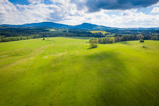Later spring time meadow scenery in south area in Czech Republic in Europe. On the horizon are hills of Novohradske hory. On the meadows are shadows of clouds.
