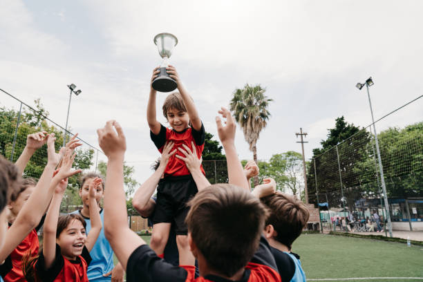 grupo de miúdos que comemoram junto com o ônibus a vitória de uma competição em um campo de futebol - soccer teenager sport adolescence - fotografias e filmes do acervo