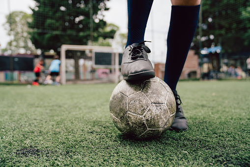 Detail of foot with soccer ball. Selective focus. Kids playing soccer in the background. Black soccer shoes.