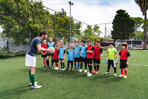 Coach encouraging kids on a soccer field. Two different sport uniforms.